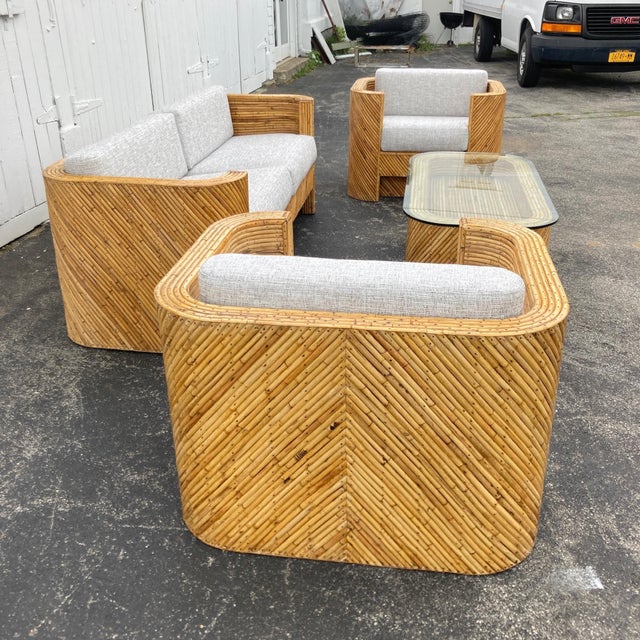 Restored and reupholstered 1940s pencil rattan sofa, pair of armchairs, and glass top coffee table. It is reminiscent of...