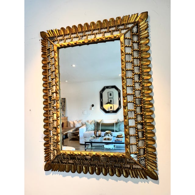 A striking rectangular mirror featuring an intricately detailed gilt frame with antiqued mirrored accents. The frame is...