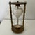 A distinctive vintage hourglass featuring a clear glass timer filled with white sand and held within an ornate three-...