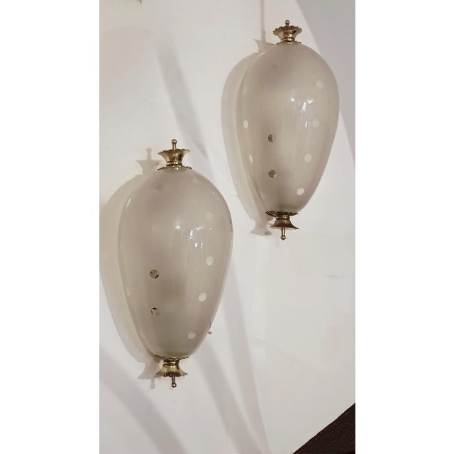 Pair of refined and delicate white Murano glass and brass wall sconces. The wall sconce has two brass wreaths, on which is...