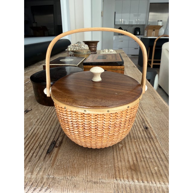 Woven white ash Nantucket basket. Maple bottom and top with natural material knob and sides. Swing handle top. Signed on...