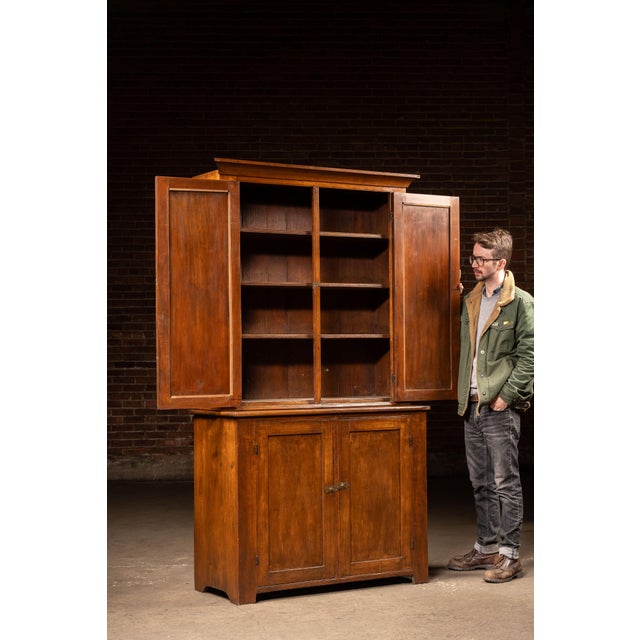 Two-piece walnut stepback cupboard featuring a recessed upper cabinet set back over a deeper lower case, creating the...
