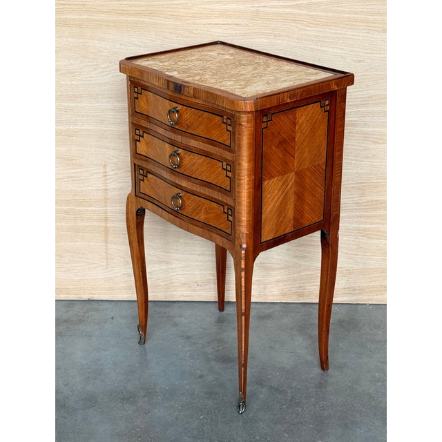 A pair of Antique French Louis XV Marquetry marble top nightstands. Subtle contours and scroll shapes are evident in the...
