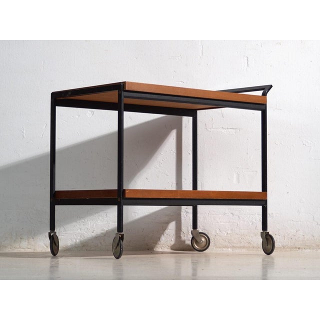 Antique opal serving trolley in wood, with a black tubular steel frame and two trays in amber-lacquered wood on swivel...