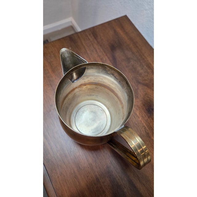 This polished brass pitcher was designed by Tommi Parzinger for Dorlyn Silversmiths in the United States circa 1960....