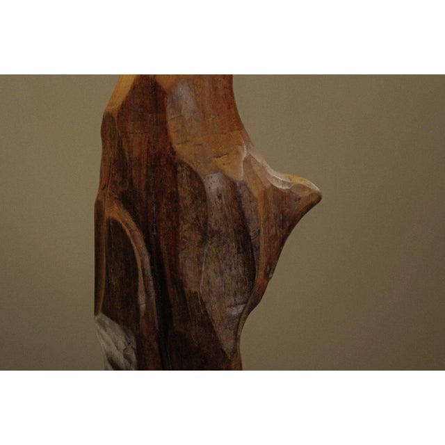 Brutalist lamp hand-sculpted from a single block of solid olive wood, revealing the warm, contrasting grain of this noble...