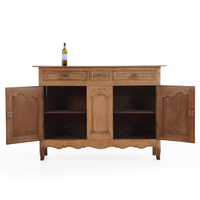 A handsome French Provincial oak sideboard featuring three drawers over two paneled cupboard doors, flanking a central...