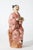 Small hand painted porcelain figurine of young Chinese woman in brightly colored floral pink attire. She is seated on a...