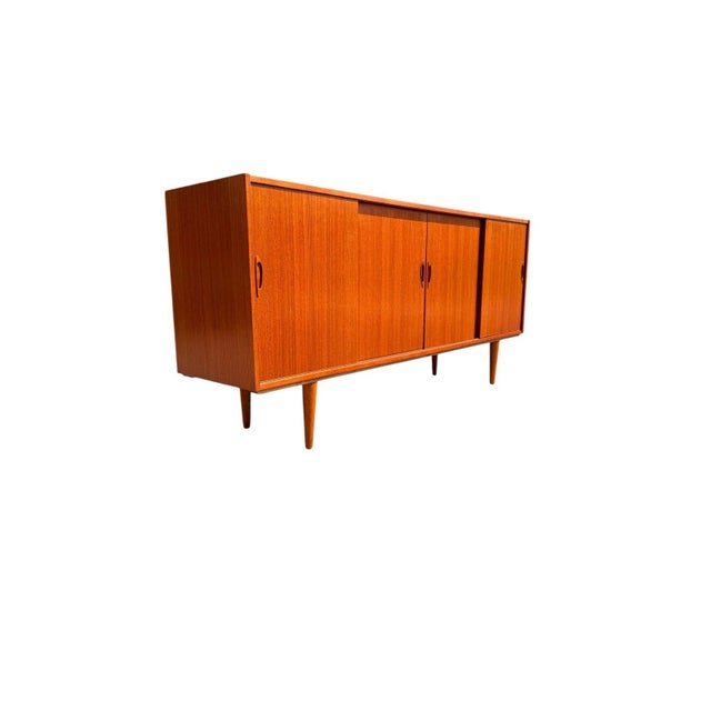 A beautifully proportioned mid-century Danish teak credenza featuring four sliding doors with sculpted teak finger-pull...