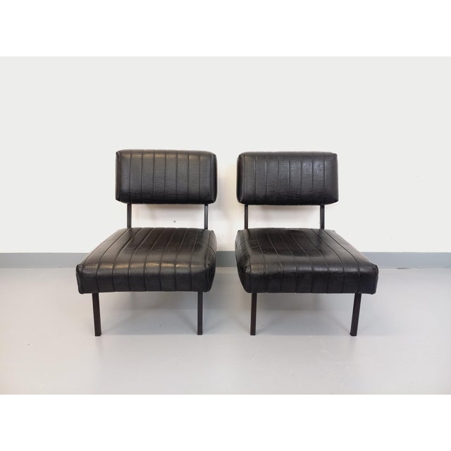 Two vintage modernist lounge chairs from the 1960s, upholstered in black quilted vinyl, with a black metal frame and...