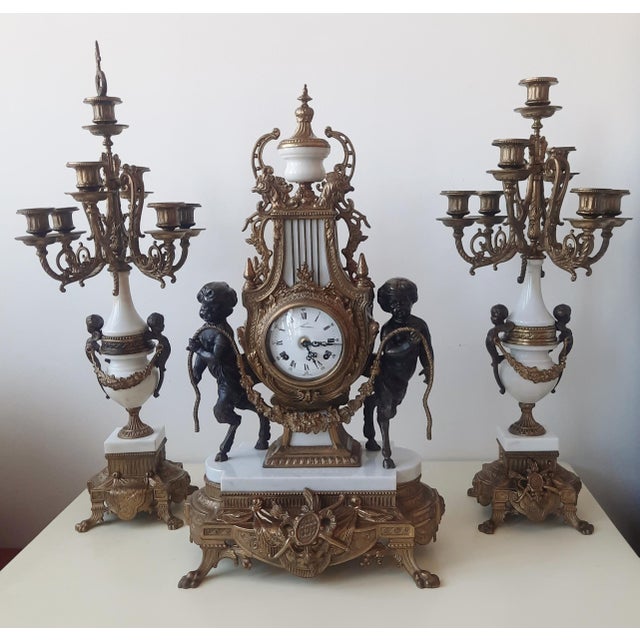 An elegant Lancini clock with a pair of Louis XVI-style candlesticks, crafted from bronze and white marble with exquisite...