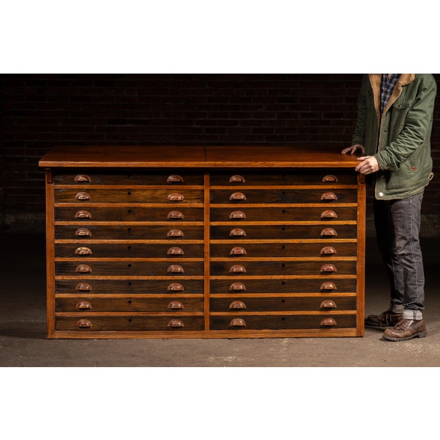 Multi-function drafting cabinet combining a slanted, height-adjustable work surface with an integrated bank of shallow...