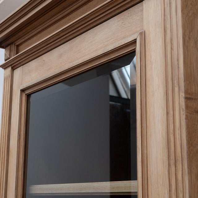 A 20th-century oak display bookcase. The upper section opens with three glass doors revealing adjustable shelves. The base...