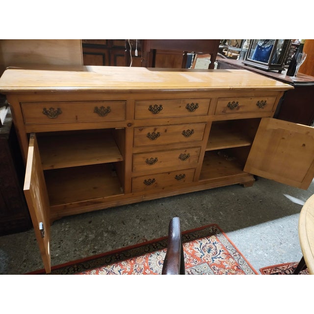 This substantial Country French–style pine sideboard showcases classic rustic craftsmanship with warm brown tones, visible...