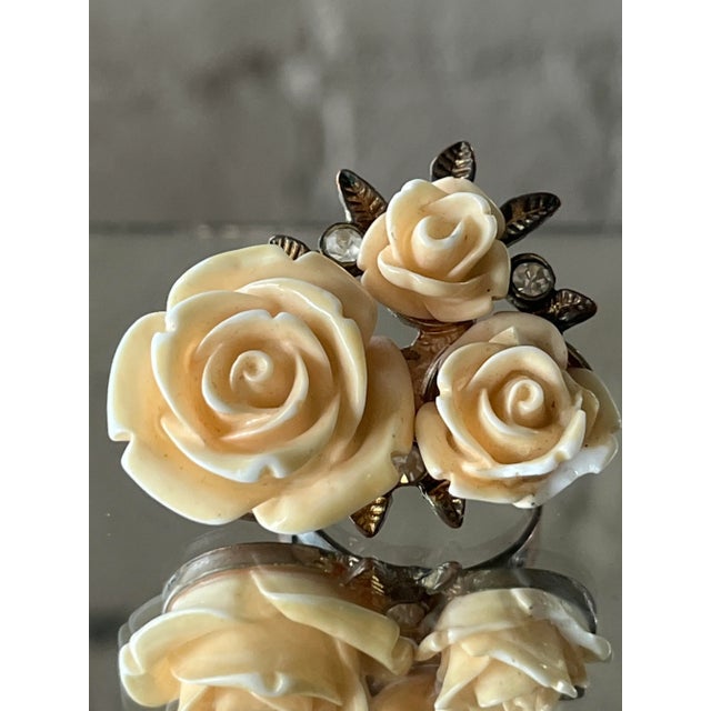 Vintage carved resin flower ring with three coral-toned roses and small rhinestone accents, set on an adjustable bronze-...