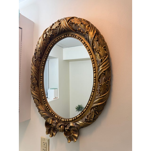 Elegant vintage style oval wall mirror with ornate antique gold finish and decorative bow detail. Made by Pinnacle Wall...