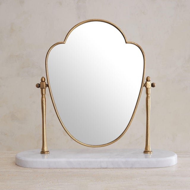 An Italian vanity mirror from the 1940s, resting on a polished oval base of white marble. Scalloped glass floats within a...