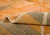 Warm horizontal bands of burnt orange, taupe, and olive shift across the surface like layered desert strata, crossed by a...