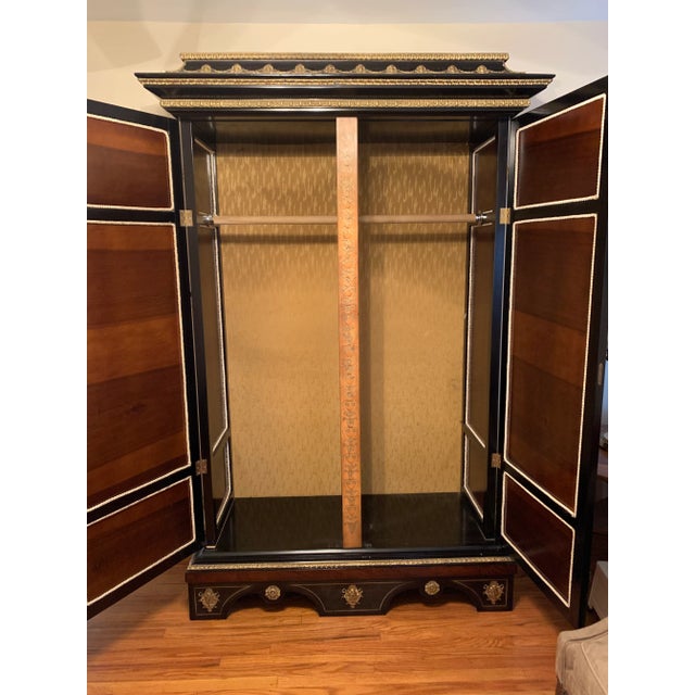 A stunning Spanish armoire featuring elaborate marquetry panels set in a black frame with brass accents. The panels are...
