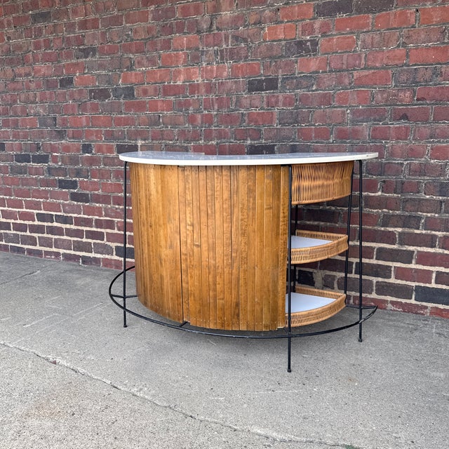 A classic Mid-Century Modern tiki bar in the style of Arthur Umanoff, featuring a curved bamboo façade, black wrought iron...
