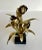 Here is a lovely, gold metal sculptural piece of a flower bouquet mounted on a black, plastic stand. The piece feels a bit...