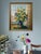 A large oil on canvas depicting a ceramic 2 tone vase at a window filled with sunflowers with a city scape in the...