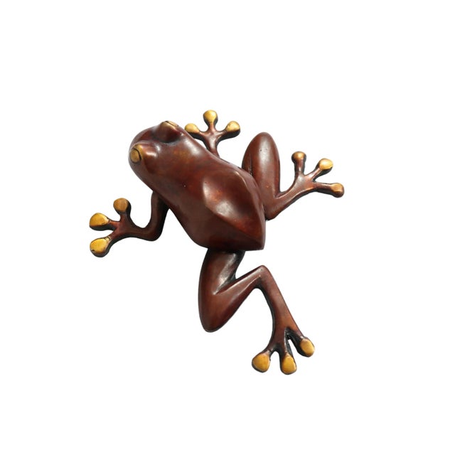 A red brass door knocker shaped like a tree frog. Cast in a climbing pose with outstretched toes, a shapely back and head...