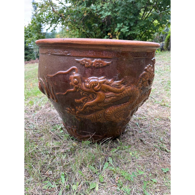 A striking vintage Chinese ceramic planter with a dramatic raised dragon motif in rich brown glaze. The dragon, a symbol...