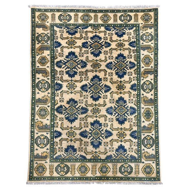 This Chobi wool rug pairs a warm cream field with repeating navy blue motifs and accents of forest green, soft gray, and...