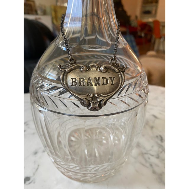 Antique hand carved crystal English decanter with a sterling silver Brandy tag. The decanter has an etched initial or...