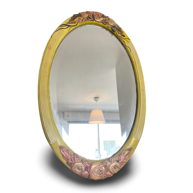 Oval wall mirror with a carved and polychrome painted wooden frame in shades of yellow and pink. The frame is decorated,...