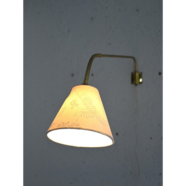 Scandinavian wall lamp with adjustable arm in golden metal. This vintage furnishing accessory is an elegant example of...