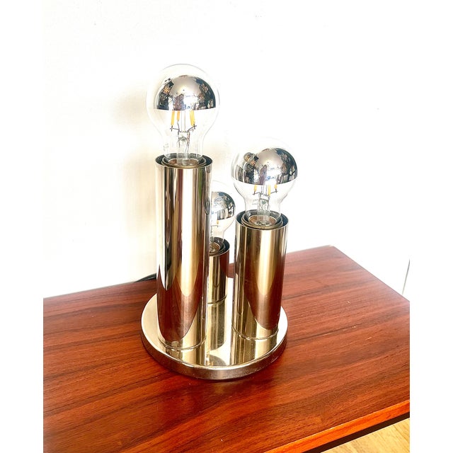 An elegant space age table lamp with a sculptural design, composed of three chromed metal tubular elements arranged in a...