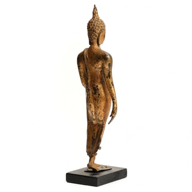 19th Century Walking Buddha figure in gilded bronze, left hand raised in abhaya mudra, mounted on a later black painted...