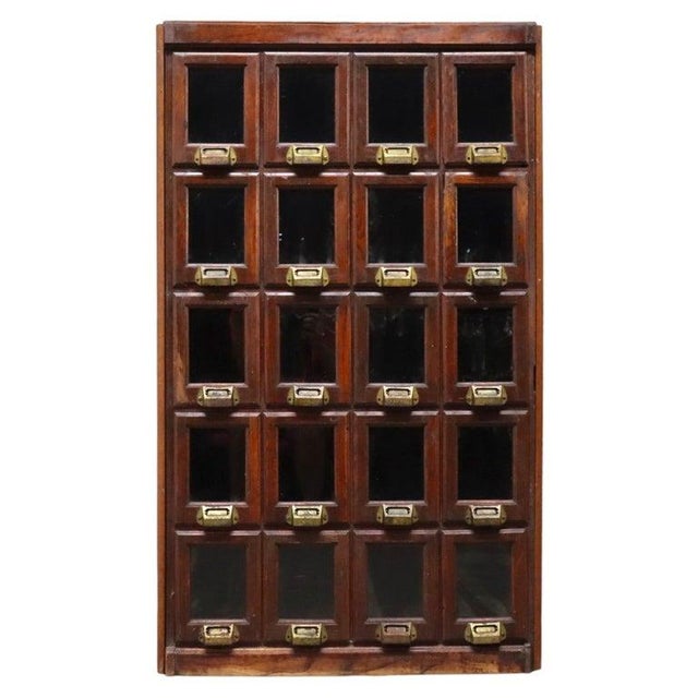 Antique oak apothecary cabinet, described as circa 1900, with 20 individual drawers arranged in five rows of four. The...
