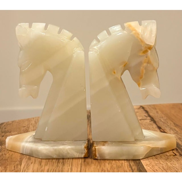 Hand-carved white and beige onyx marble bookends fashioned into a pair of horse heads. These stylized horse heads are...