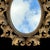 This ornate oval wall mirror is crafted in a Baroque or Rococo Revival style and dates to the early 20th century, a form...