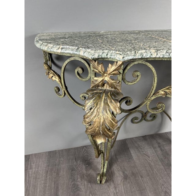 Wrought iron wall console, adorned with gilded scrolls and foliage, topped with a veined marble slab. The wrought iron...