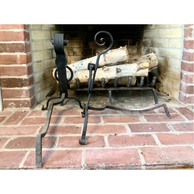 A pair of hand-forged wrought iron Arts & Crafts style andirons with cylindrical scroll-top finials, ring-loop mid-section...