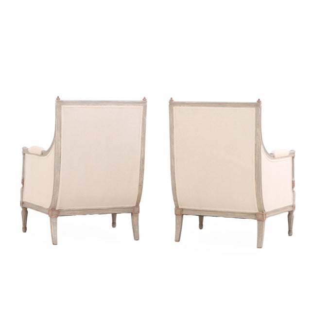 Refined pair of Louis XVI style bergère chairs constructed in gray-painted wood with partial gilt highlights. Each chair...