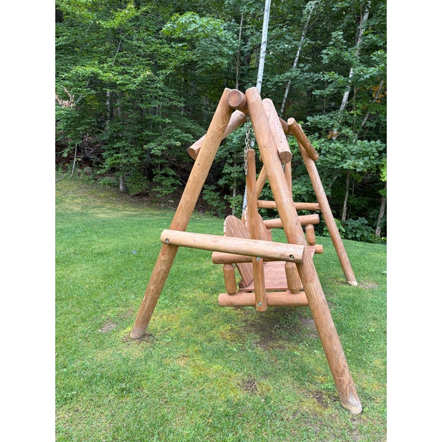 Substantial rustic outdoor swing featuring a freestanding solid log frame and a generously sized double seat with...
