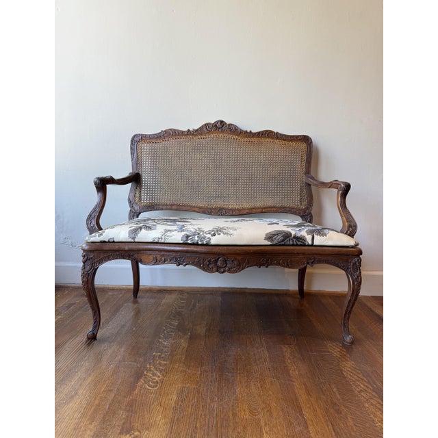An elegant 1870 Louis XV settee featuring a caned wicker back, a carved European frame, and newly upholstered neutral...