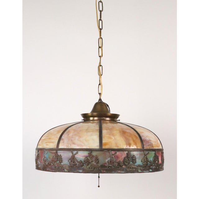 1910s pendant light with a slag glass shade with a repetitive windmill motif paired with an antique brass fitter and pull...