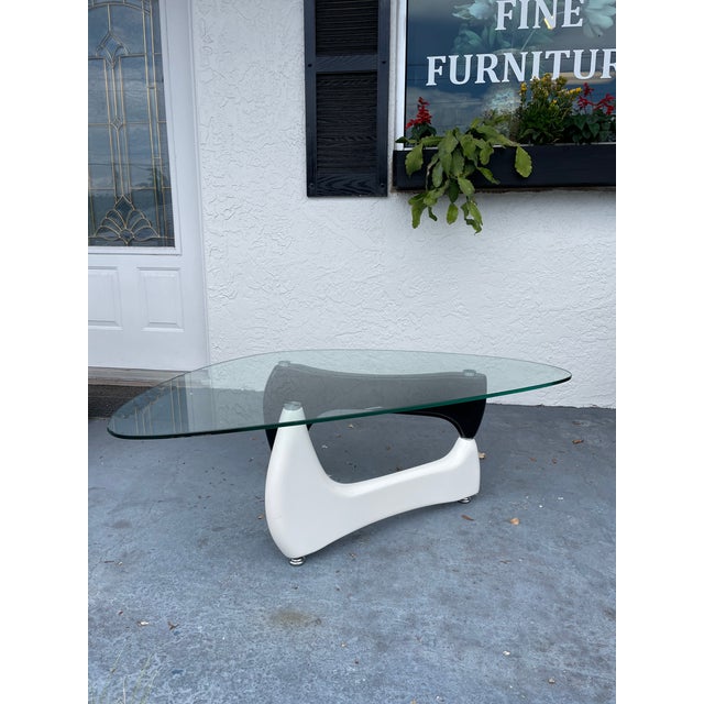 A striking sculptural coffee table featuring a uniquely shaped tempered glass set atop a bold black and white base....