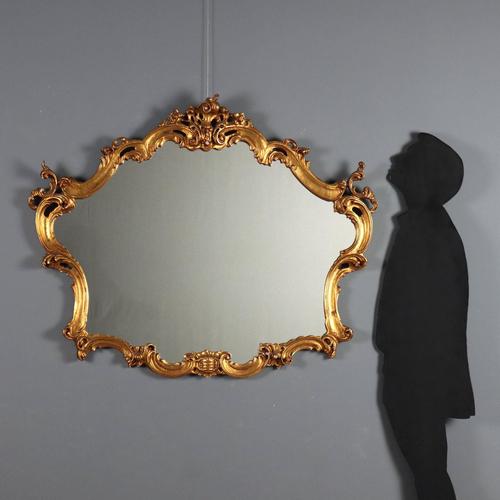 Baroque-style mirror in carved and gilded wood. Frame with carved scrolls, curls, and flowers. Small losses. Italy, 20th...