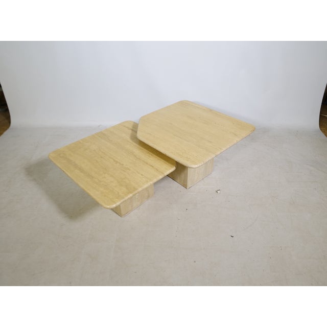 Two-piece nesting table set made of travertine with square tabletops and slightly beveled corners. The tables, of varying...
