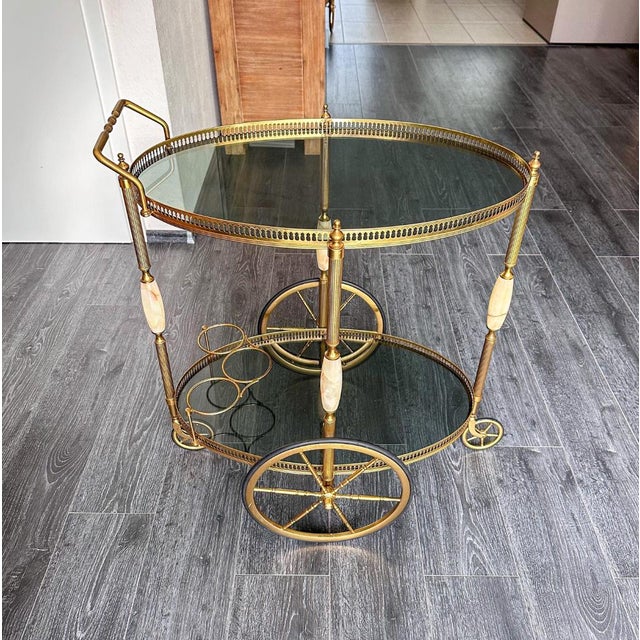 This elegant vintage brass serving cart features an oval shape, decorative brass galleries, natural onyx inlays, and two...