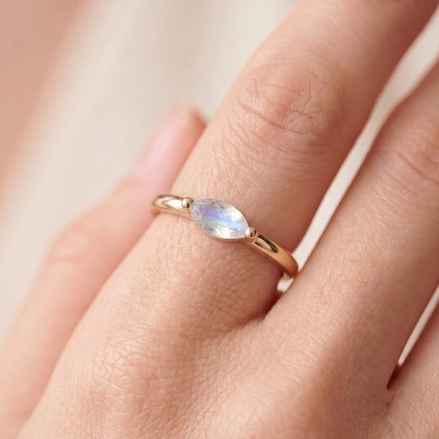 An ethereal, minimalist solitaire featuring a marquise-cut moonstone with a soft blue glow set in an east-west...