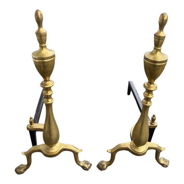 Pair of Antique 1920s brass andirons in the Chippendale style featuring elegant finials and classic claw and ball feet....