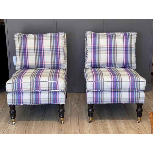 A pair of vintage custom-upholstered English-style slipper chairs displaying low backs and armless forms with loose seat...